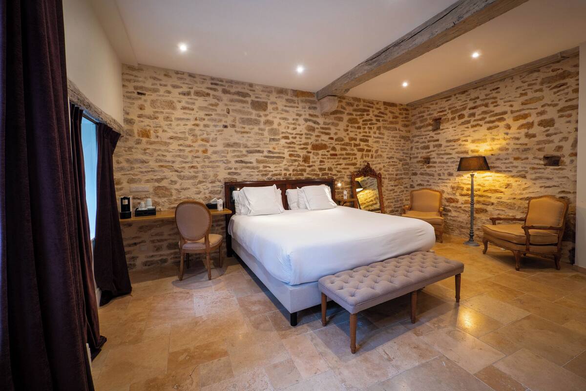 Ein Schlafzimmer mit Steinwand, einem hölzernen Bett, einer Bank, einem Stuhl und einem Schreibtisch mit Lampe.