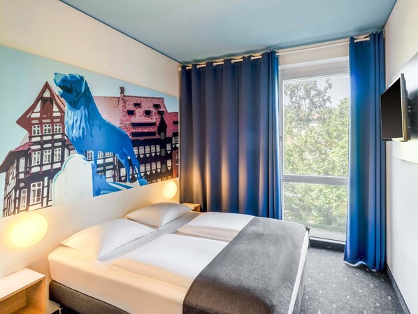 Quarto de hotel com cama, painel decorativo na parede, janela com cortinas e televisão de tela plana.