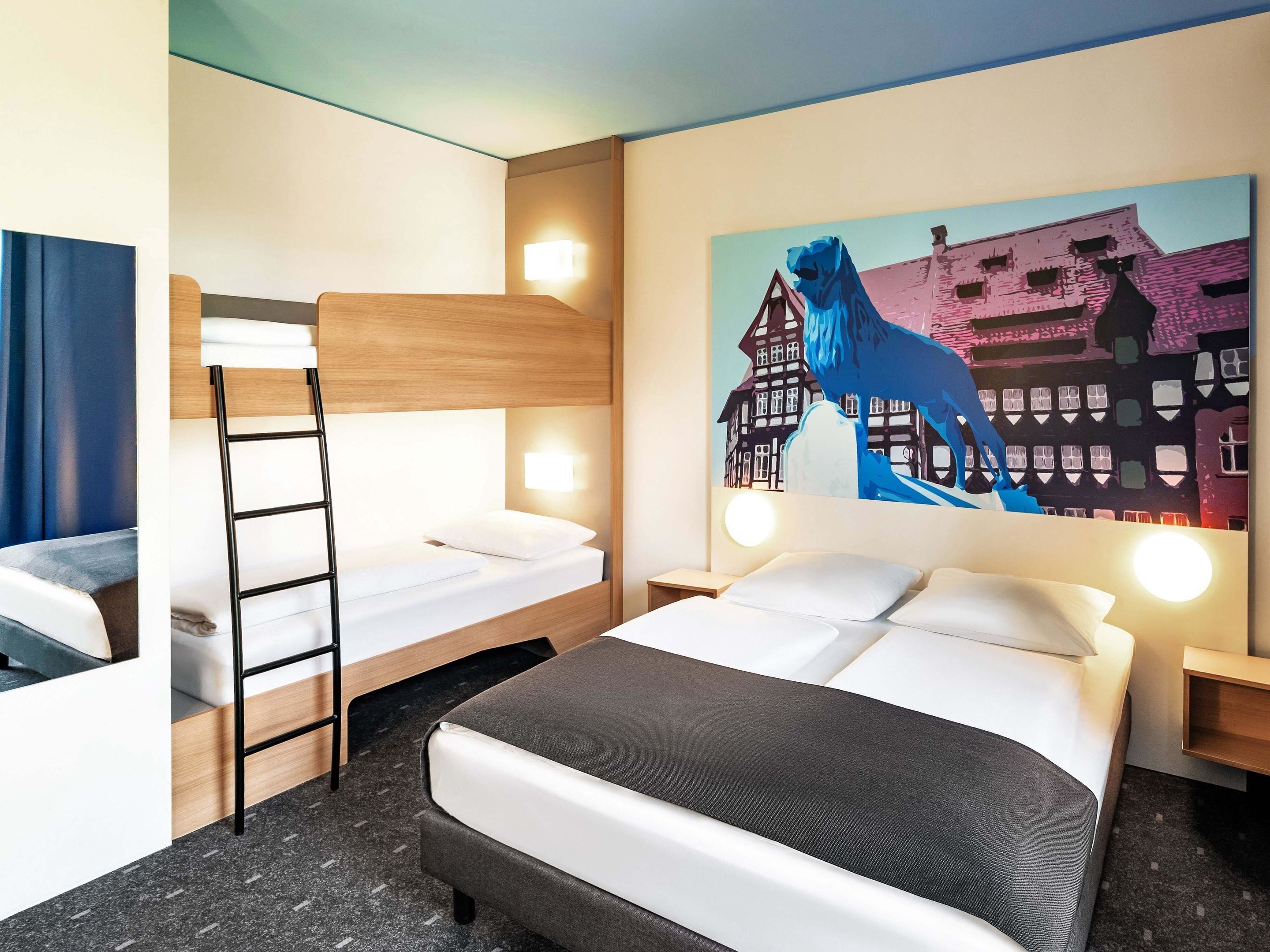 Une chambre d’hôtel avec un lit superposé, un bureau et un tableau représentant un cheval et des bâtiments.
