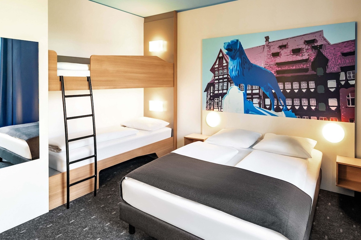 A hotel room with a bunk bed, a desk, and a painting of a horse and buildings.