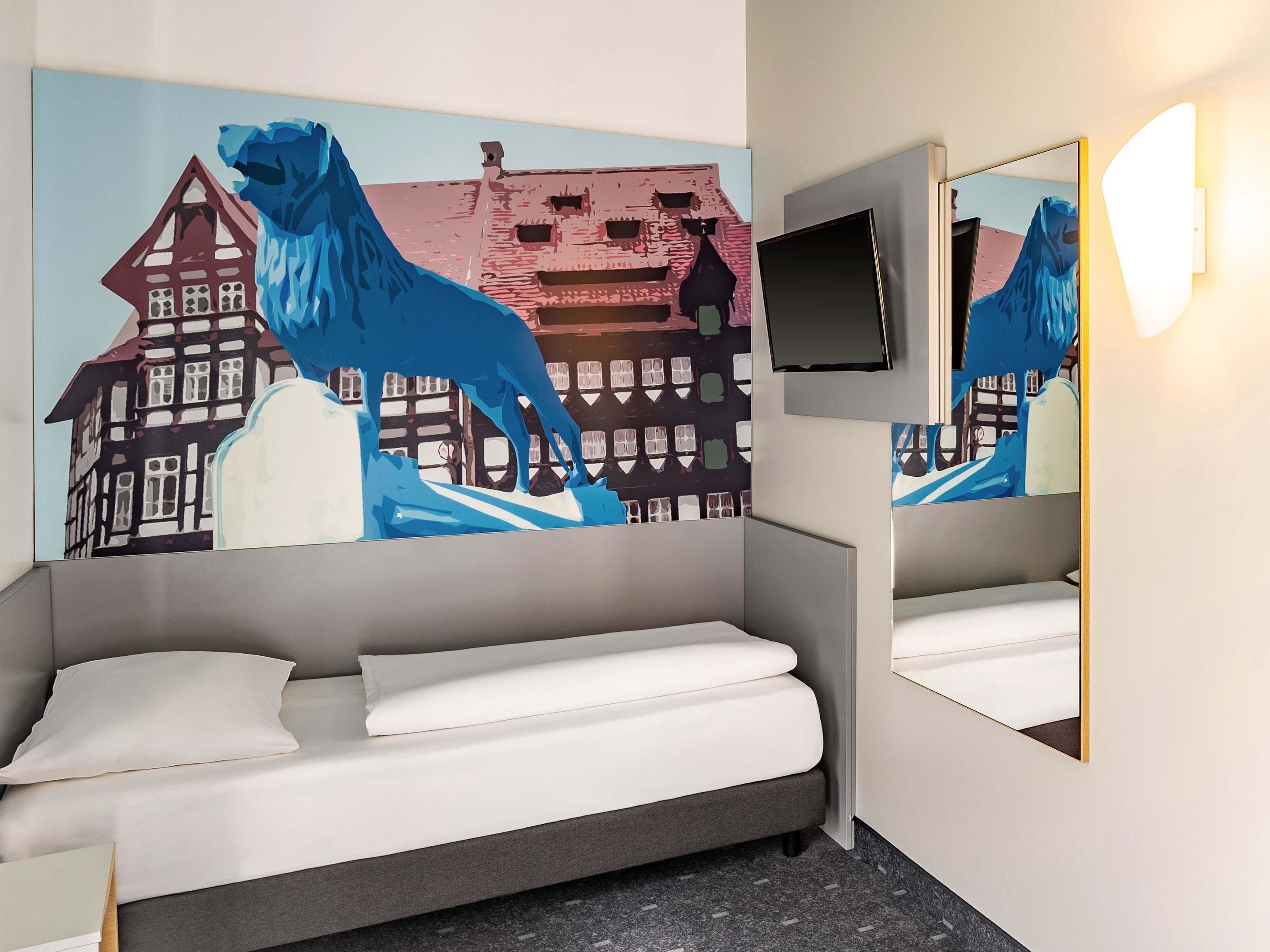 Una habitación de hotel con una cama, un cuadro grande de un león azul y un televisor montado.
