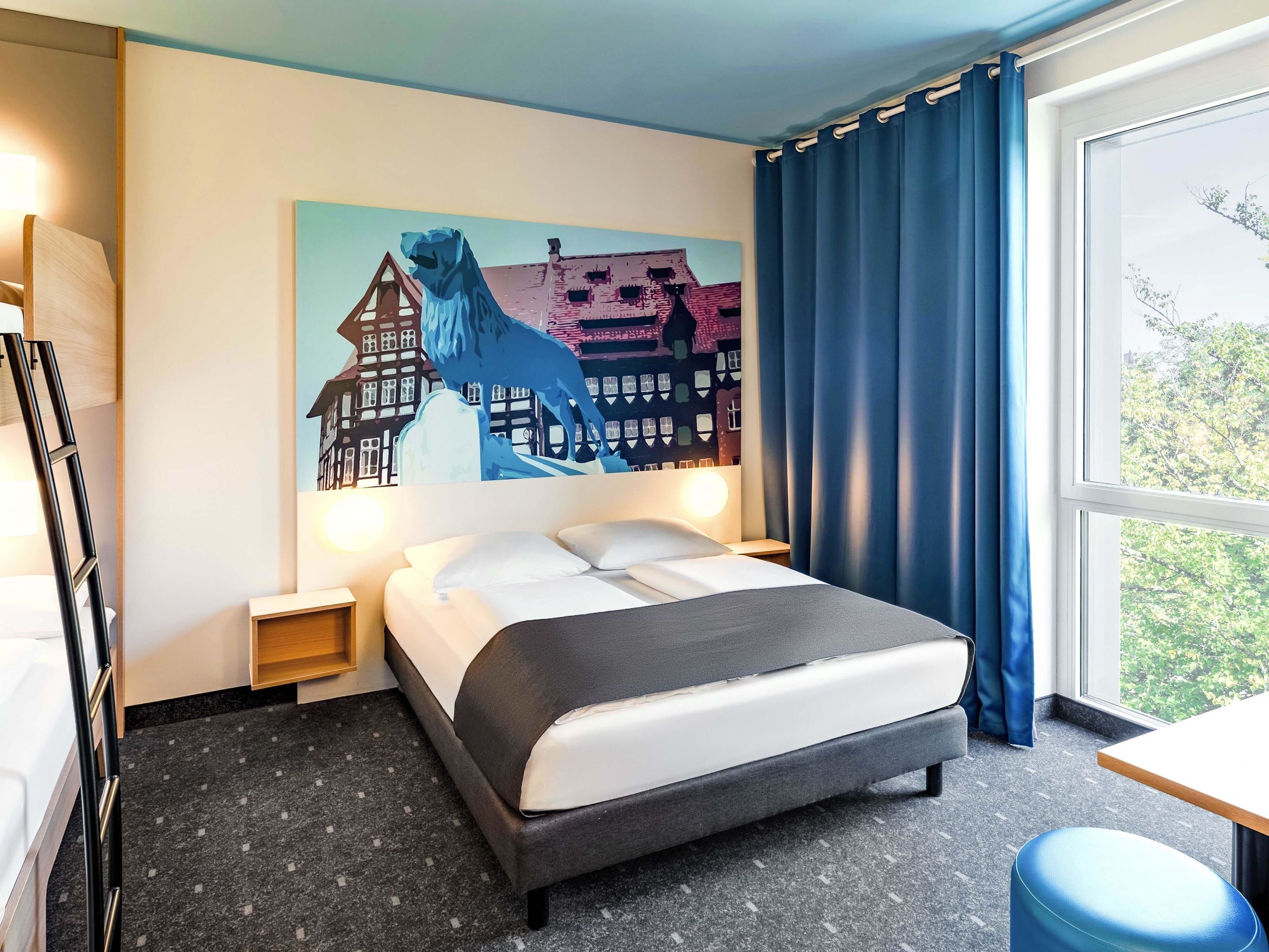 A hotel room with a bed, a nightstand, a lamp, a painting of a horse and buildings, and a window with curtains.