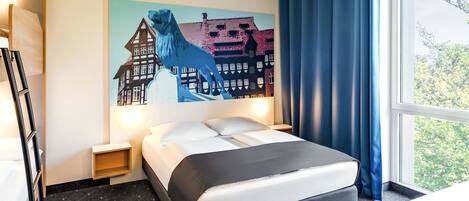 Una habitación de hotel con una cama, una mesita de noche, una lámpara, un cuadro que muestra un caballo y edificios, y una ventana con cortinas.