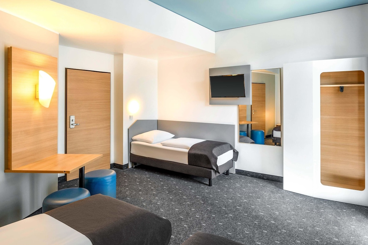 A modern hotel room with a bed, a desk, a chair, a TV, and a mirror.