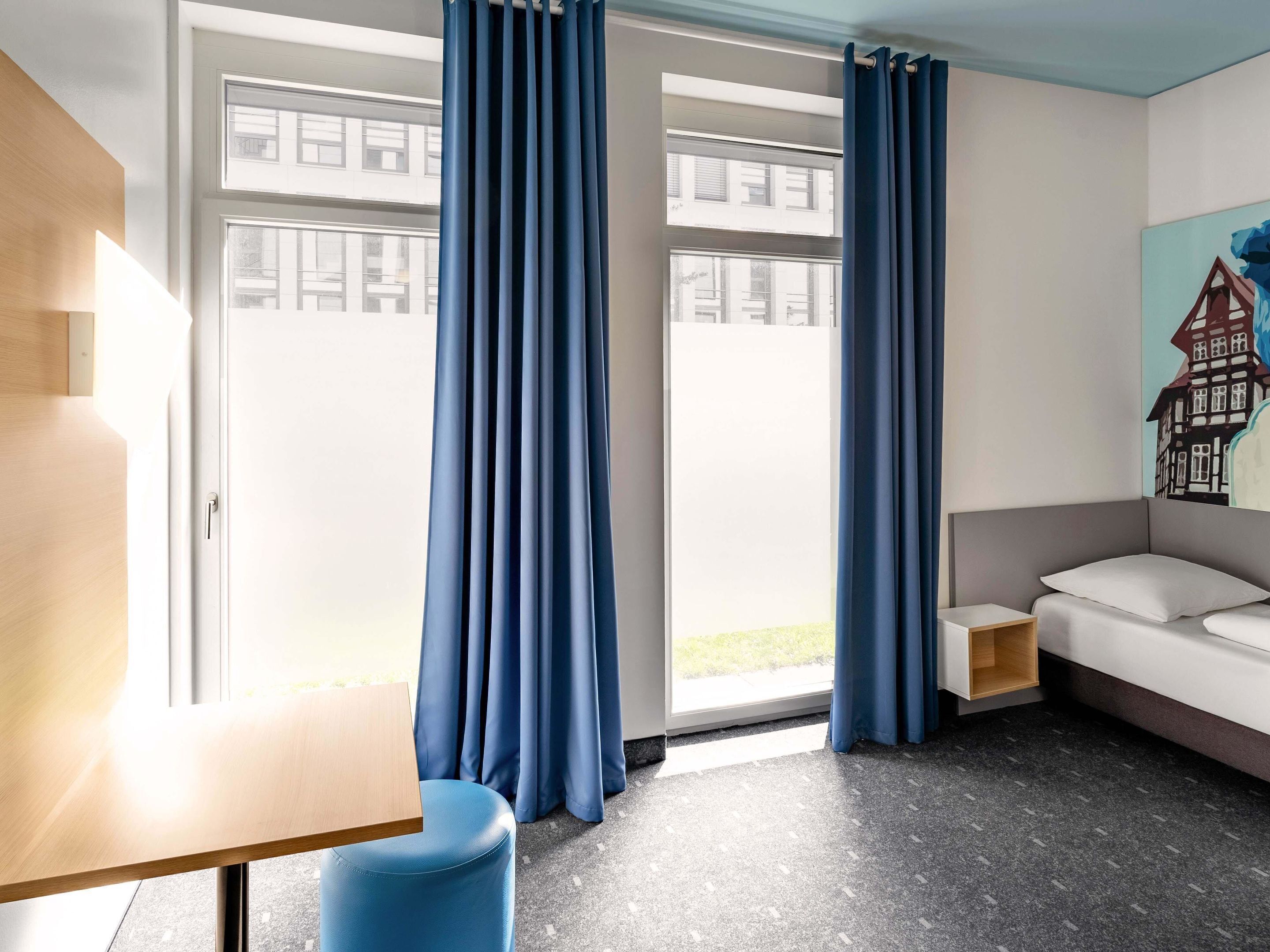 Ein modernes Zimmer mit großem Fenster, Schreibtisch, Sofa und einem Gemälde an der Wand.