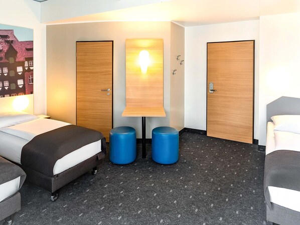 Una habitación de hotel con dos camas, una lámpara fijada a la pared y dos taburetes azules.