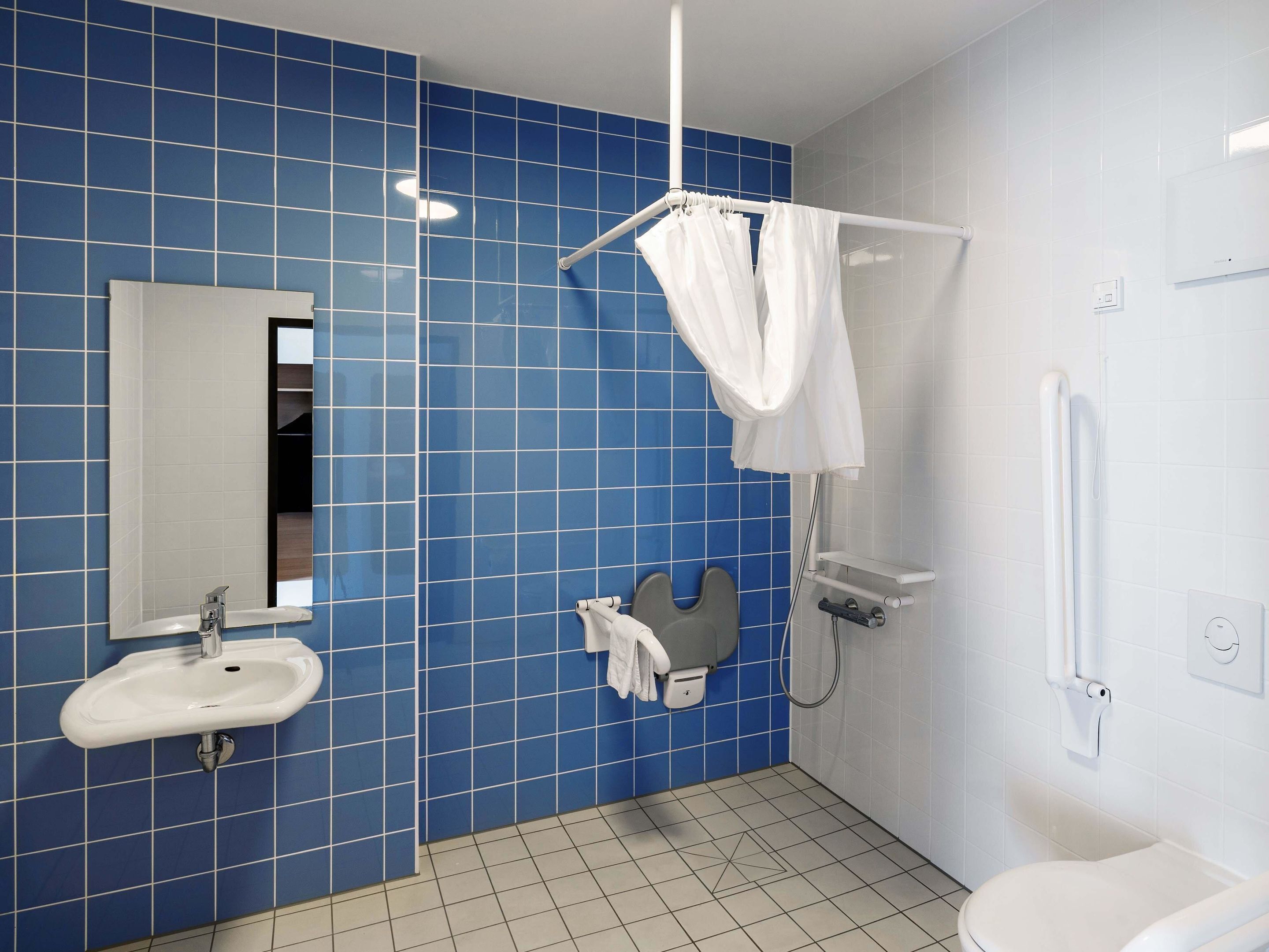 Et badeværelse med blå klinkevægge, en hvid vask, et spejl, en bruser og et toilet.
