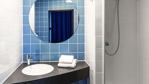 Un baño con un espejo redondo, un lavabo y una ducha.