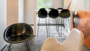 Een moderne vergaderruimte met een witte tafel en vier zwarte stoelen, plus een witte stoel, en een grote abstracte muurschildering op de wand.