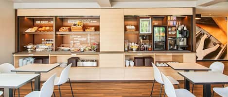 Ein moderner Frühstücksbereich mit Buffet, Kaffeeautomat und Sitzgelegenheiten.