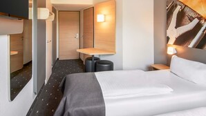 Een hotelkamer met een bed, nachtkastjes, een bureau, een stoel, een lamp en een tv aan de muur.