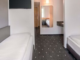 Quarto de hotel com duas camas, televisão, espelho e banheiro visível por uma porta aberta.