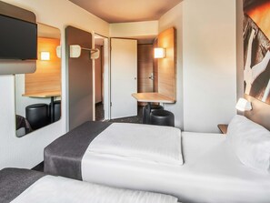 A hotel room with a bed, a TV mounted on the wall, a mirror, and a small table with a lamp. - B&B Hotel Offenbach-Süd (Offenbach am Main)