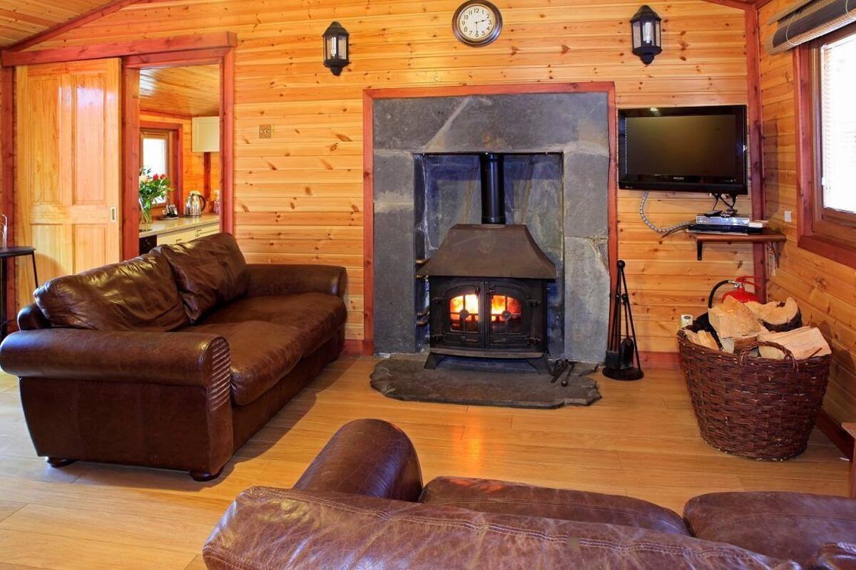 A cozy cabin interior with a stone fireplace, leather furniture, and a television mounted on the wall.