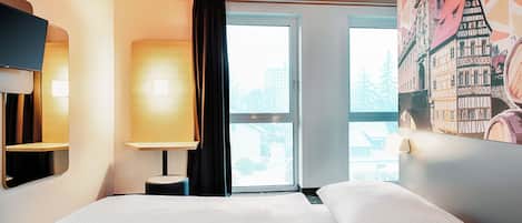 Habitación de hotel con cama, escritorio, silla, televisión y una ventana grande con vistas a edificios.