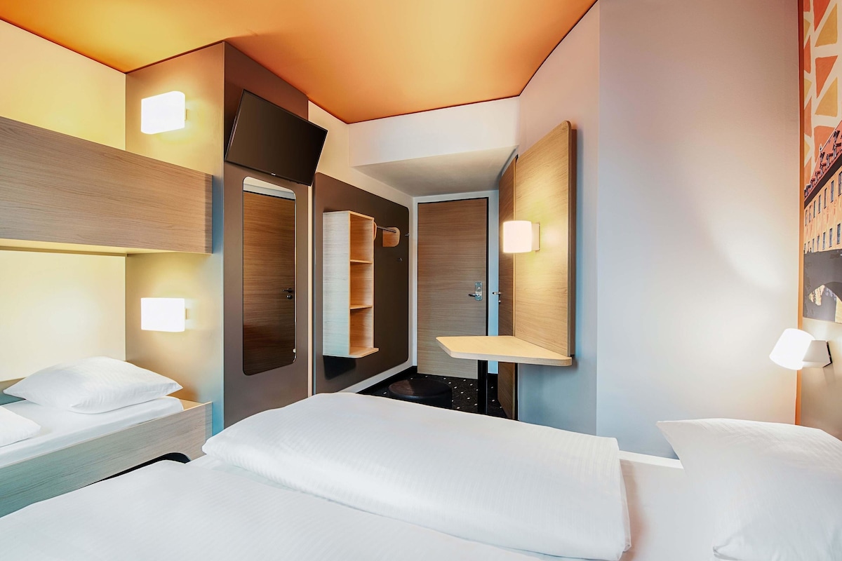 Una habitación de hotel moderna con una cama, mesitas de noche, un espejo y estanterías empotradas.
