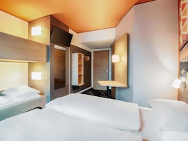 Una habitación de hotel moderna con una cama, mesitas de noche, un espejo y estanterías empotradas.
