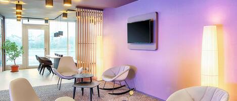 A modern lounge area with contemporary furniture, a flat-screen TV, and a view through large windows.