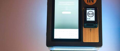 A self-check-in kiosk with a digital screen and a mobile device interface for B&B Hotels.