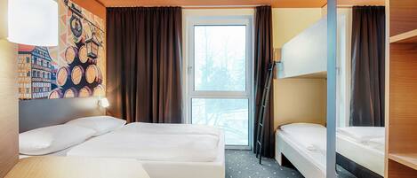 Habitación de hotel con cama, escritorio, silla, ventana con cortinas y literas.