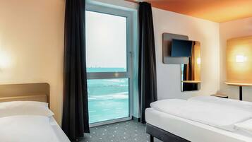 Una habitación de hotel con dos camas, un ventanal con cortinas, un televisor de pantalla plana y una pequeña mesa.