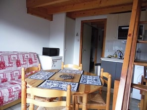 Un'area pranzo con un tavolo e sedie in legno, un divano a due posti con motivo rosso e bianco, un forno a microonde e una cucina sullo sfondo.