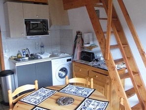 Una cucina funzionale con forno a microonde, lavello e lavatrice. Si nota un tavolo di legno con sottopiattino e una sedia. Sullo sfondo, una scala in legno.
