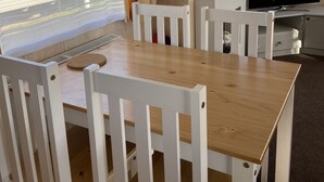 Een kamer met een houten tafel, witte stoelen, een televisie en beige gordijnen.