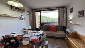 Zona de menjador acollidora amb una taula preparada per a quatre, una panxa de fusta i un sofà amb coixins. Una finestra ofereix vistes a la verdura a l'exterior.