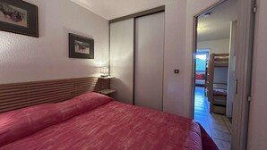 Un dormitori amb un llit, una taula de nit amb una làmpada, un quadre amb marc a la paret i una porta que dóna a un balcó amb un llit superposat.