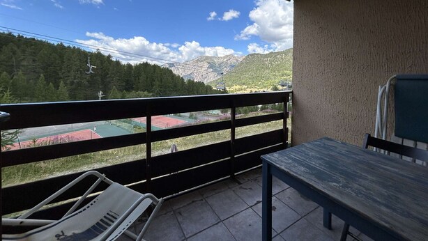 Un balcó amb vista a una pista de tennis, muntanyes i un teleàsics.