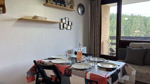 Zona de menjador amb taula preparada per a quatre, un rellotge a la paret i vista a zones verdes a l'exterior.