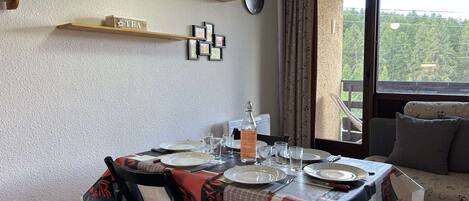 A dining area with a table set for four, a clock on the wall, and a view of greenery outside.