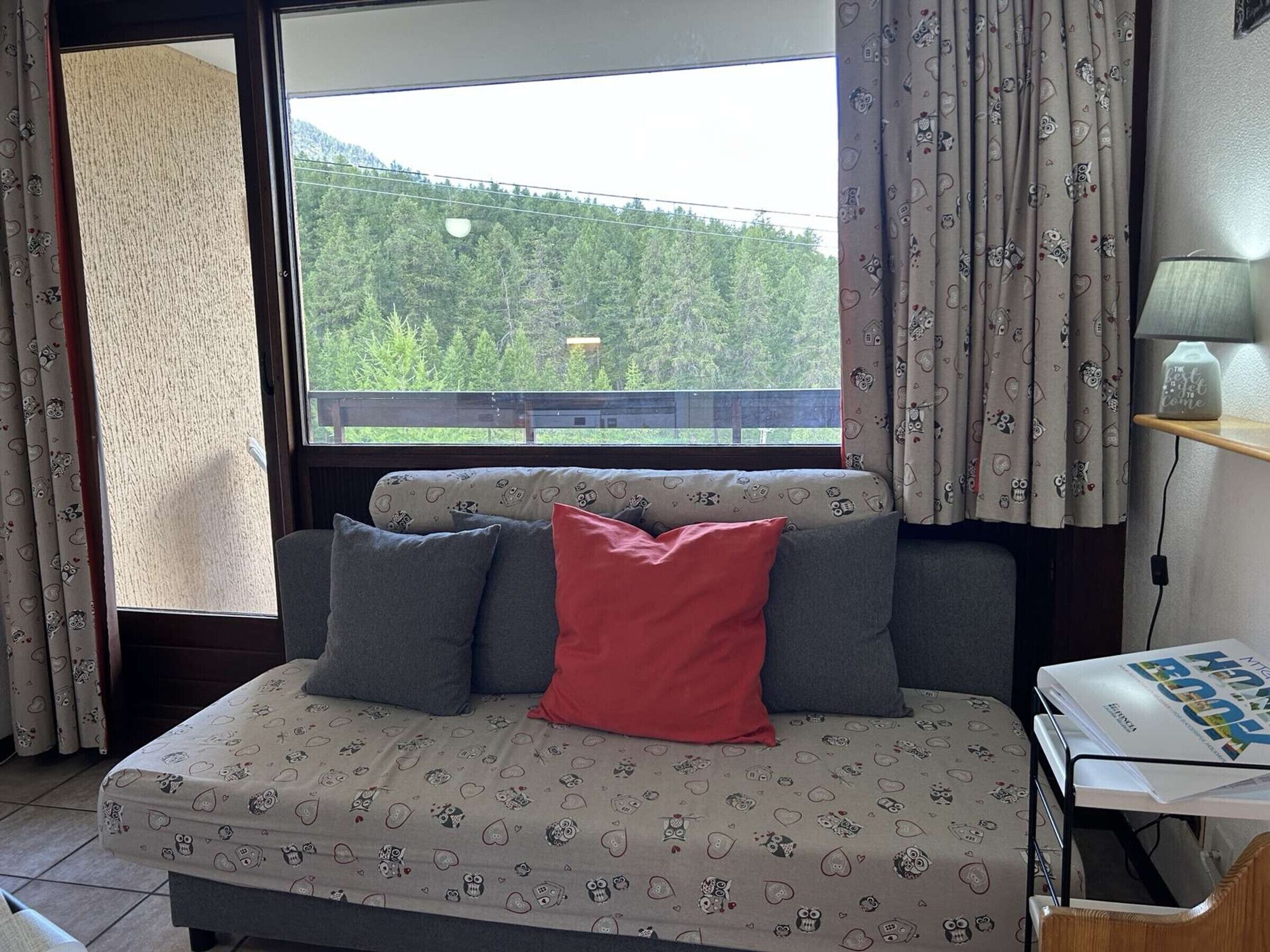 Une chambre à coucher avec un lit, une fenêtre avec des rideaux, une lampe et une vue sur une forêt.