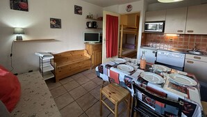 Una cuina compacta amb una taula de dinar a punt per a quatre persones, microones, rentapelats i un refrigerador petit.