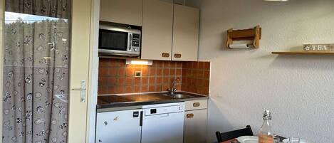 A compact kitchen with a microwave, sink, and a dining area set for four.