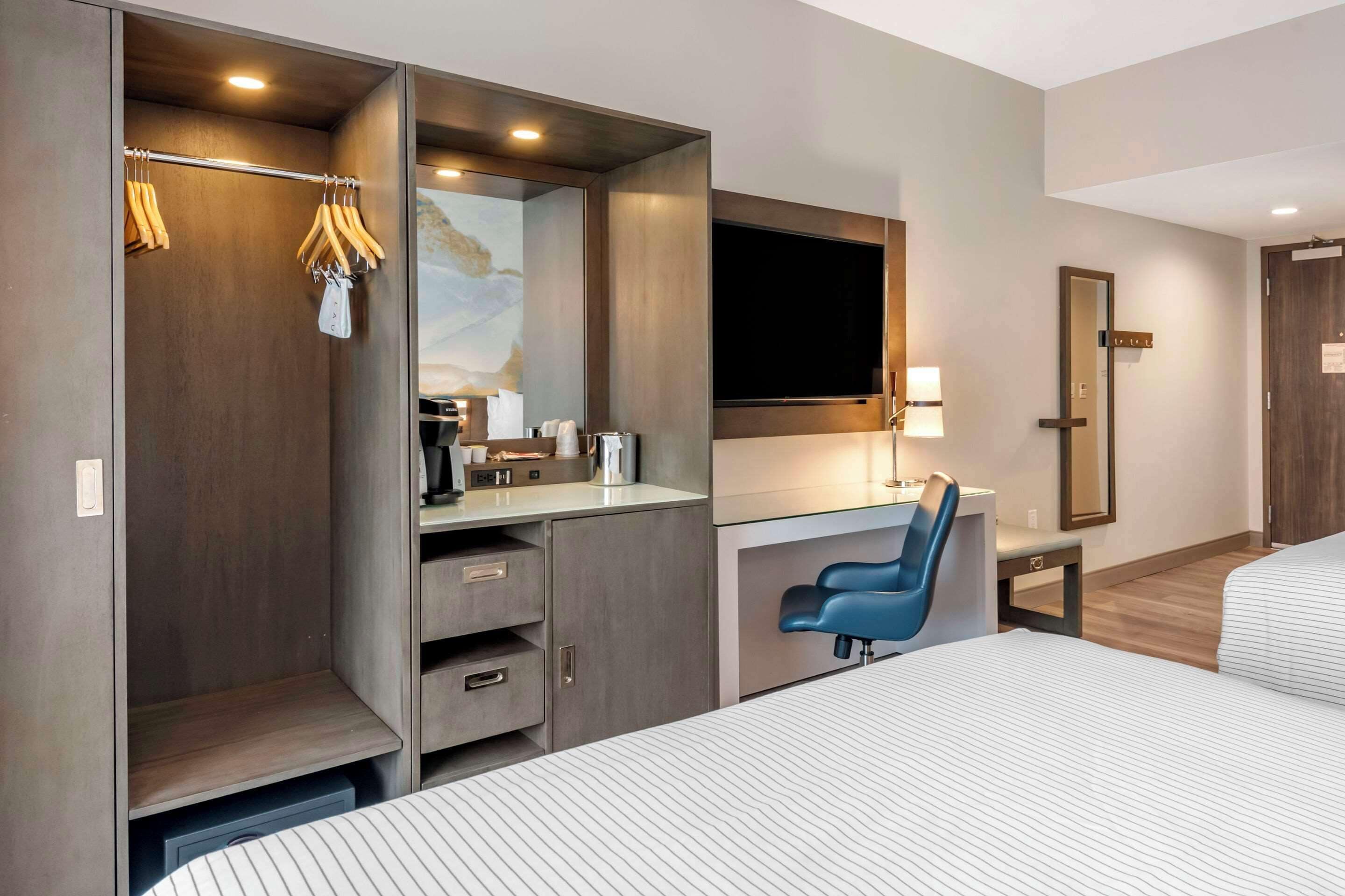 A modern hotel room with a bed, a desk with a chair, a wardrobe, and a television.