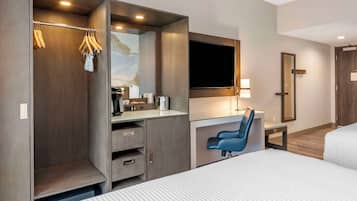 A modern hotel room with a bed, a desk with a chair, a wardrobe, and a television.