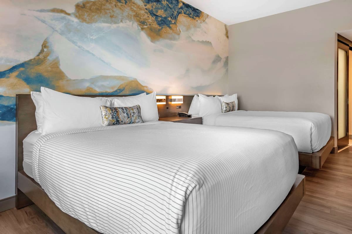 A hotel room with two beds, a large abstract mural on the wall, and a wooden floor.