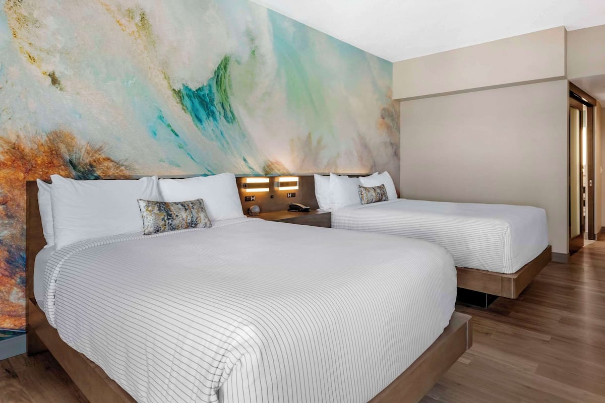 A hotel room with two beds, a large abstract mural on the wall, and a wooden floor.