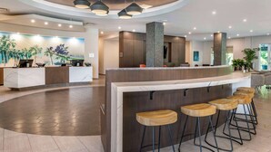 A modern reception area with a curved counter, wooden bar stools, and pendant lighting. - Cambria Hotel Orlando Airport (Orlando)