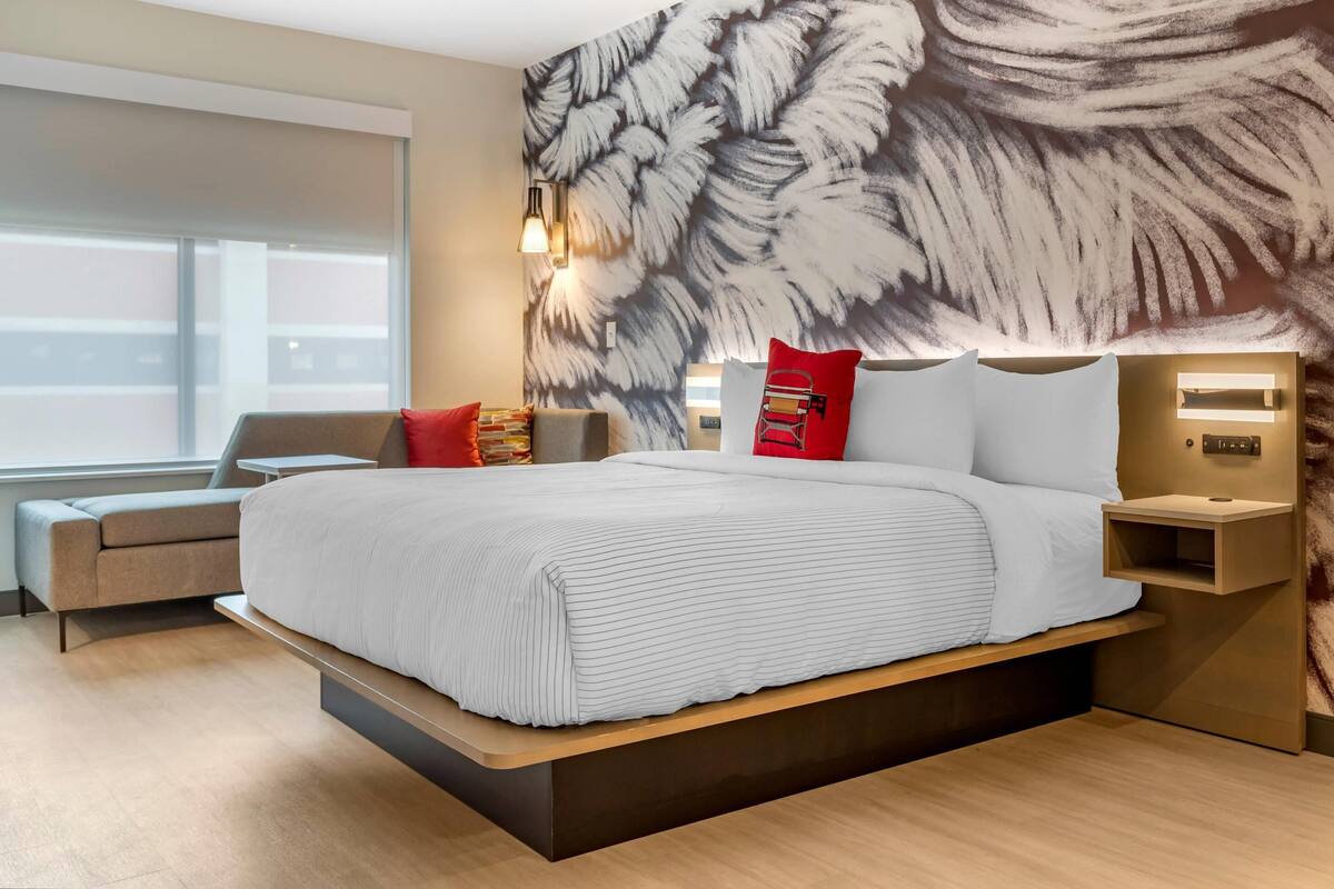 A modern hotel room with a large bed, a sofa, a nightstand, and a wall with a leaf pattern.
