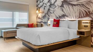 Quarto de hotel moderno com uma cama grande, um sofá, uma mesa de cabeceira e uma parede com padrão de folhas.