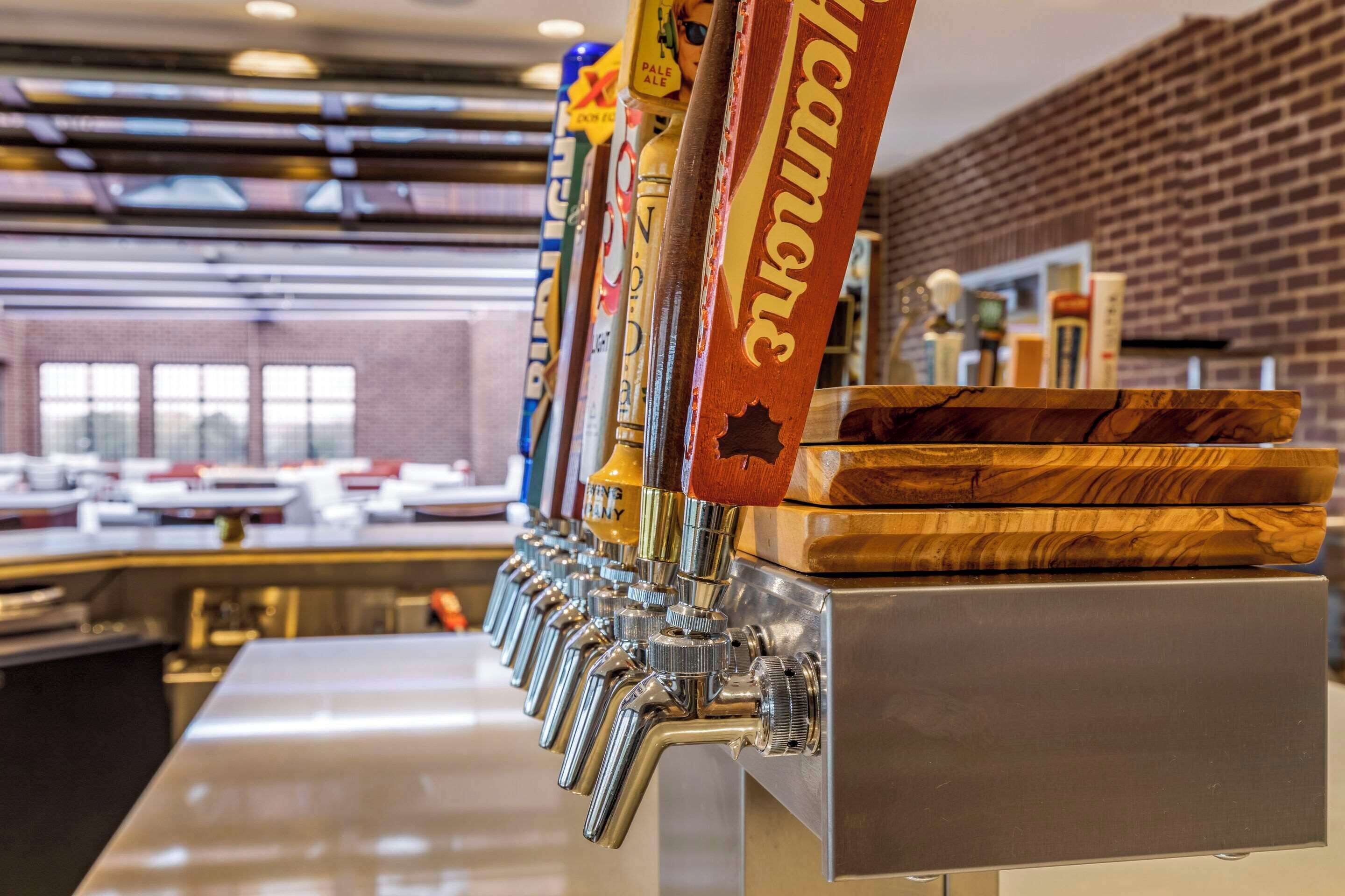 A row of beer taps with labels, a brick wall, and a counter in the background.