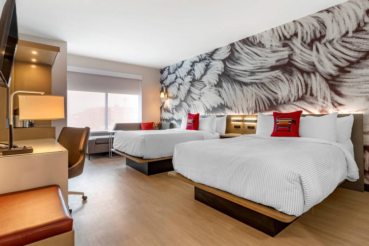 A hotel room with two beds, a desk, a chair, and a large window.