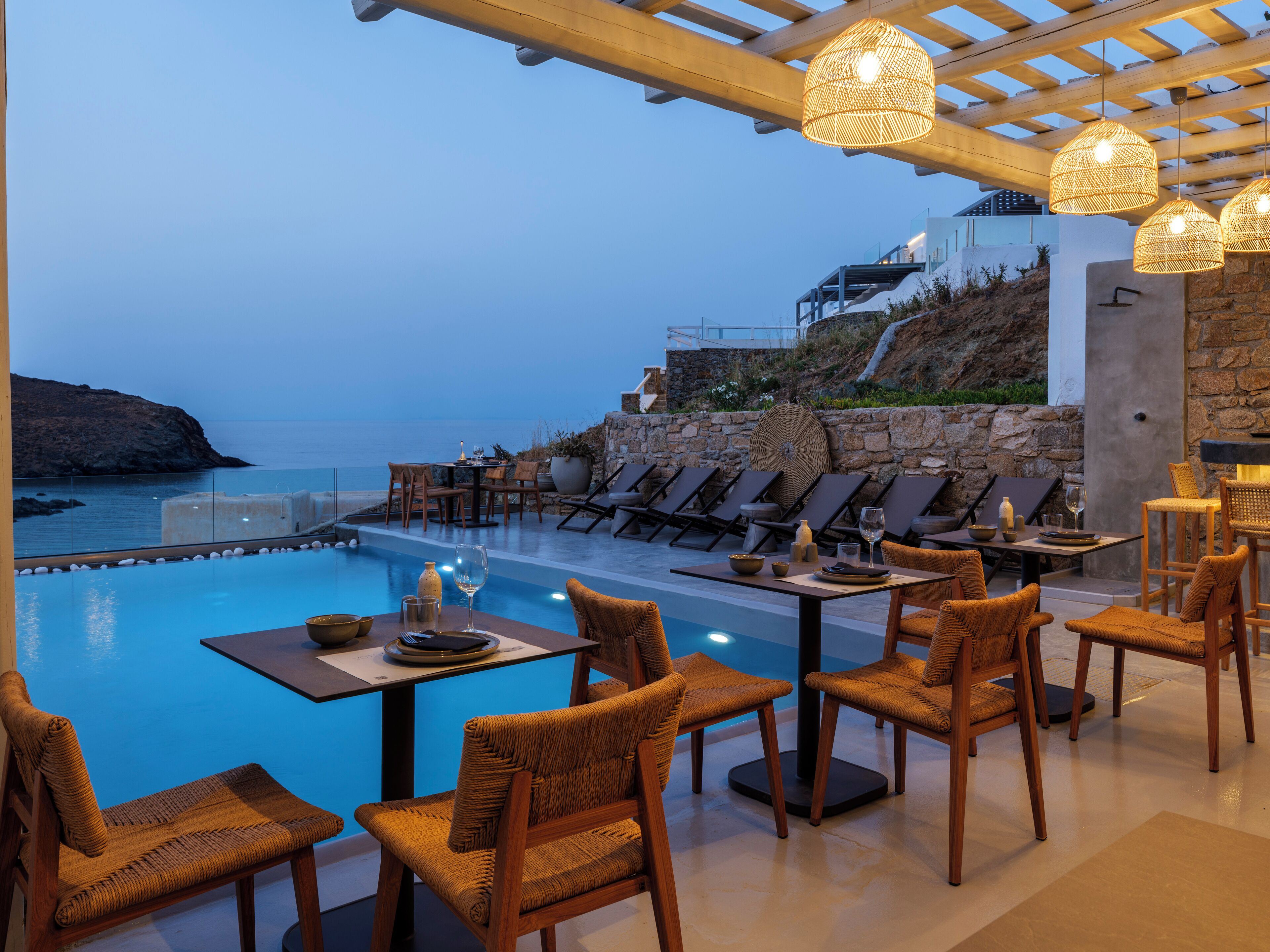 A poolside dining area with chairs and tables, overlooking a pool and a coastal view.