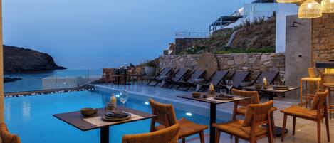A poolside dining area with chairs and tables, overlooking a pool and a coastal view.