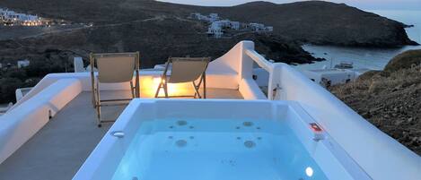 A hot tub with two chairs, overlooking a coastal landscape with buildings in the background.