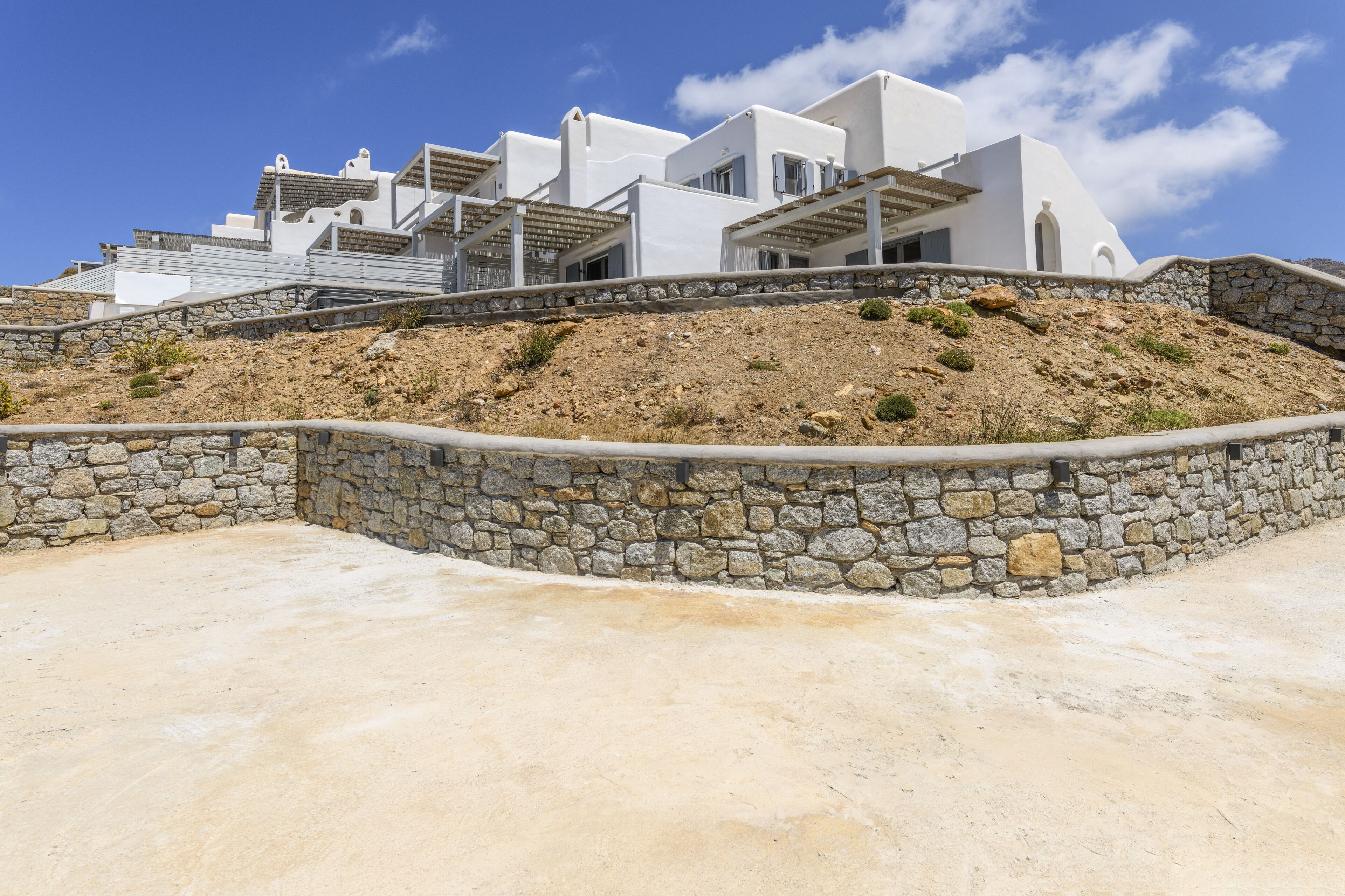 Un edificio moderno de color blanco con paredes de piedra y techo inclinado, ubicado en una ladera.