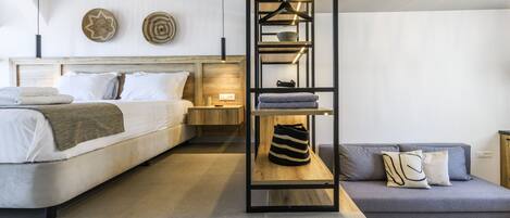 A modern bedroom with a bed, a grey sofa, a wooden shelf with clothes, and a hanging rack.